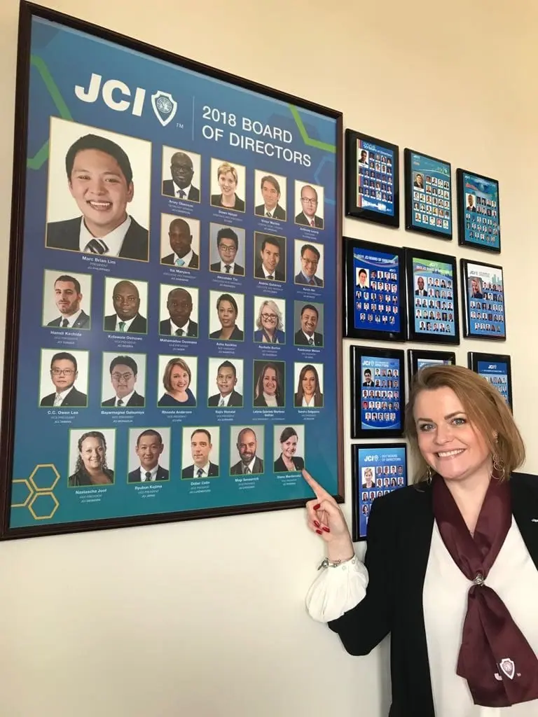 A woman pointing at a wall of portraits of the 2018 JCI board of directors