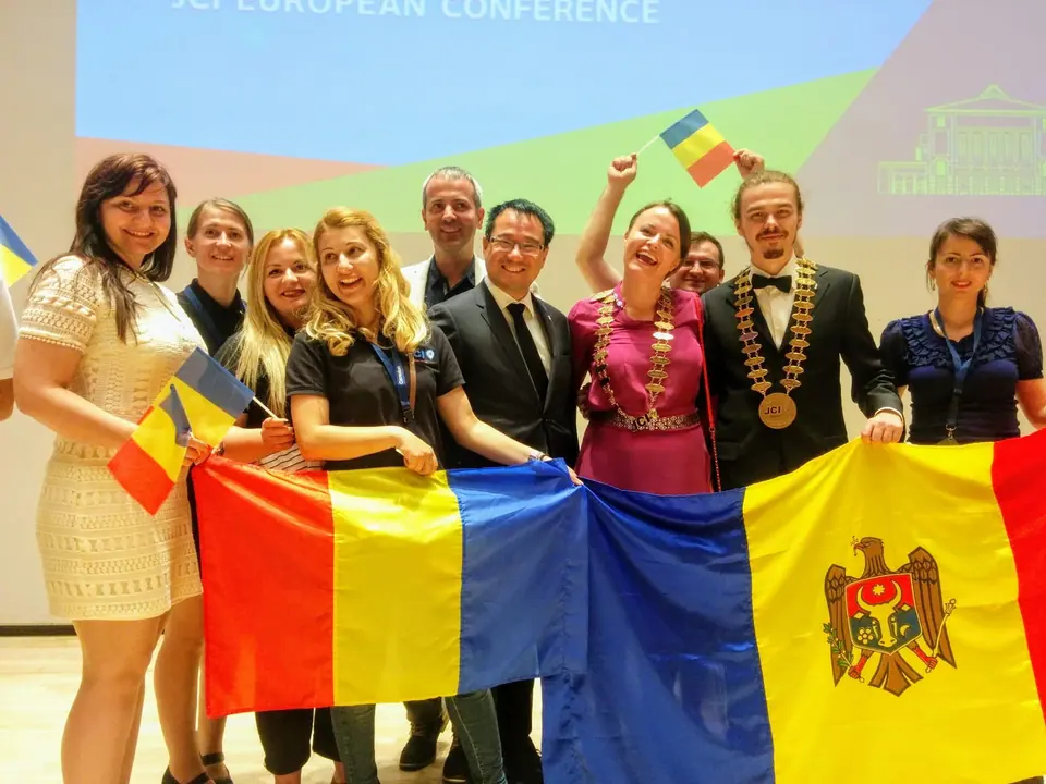A smiling group holding Romanian and Moldovan flags on a conference stage