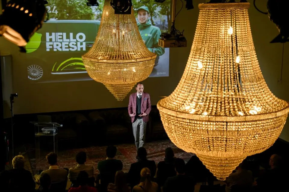 Stef Verbeeck on a stage beneath two large crystal chandeliers, with a Hello Fresh slide behind him