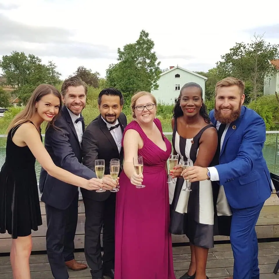 Six people in evening dress toasting with champagne glasses by a lake