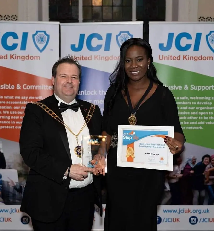 A man and a woman in chains of office holding an award certificate in front of JCI United Kingdom banners