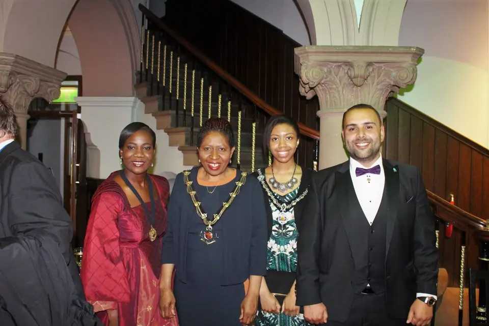 Four people in formal wear, two of them wearing chains of office, on a stone staircase landing