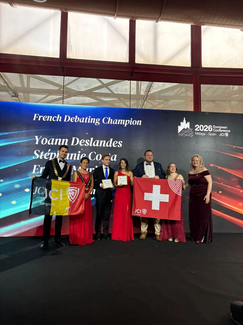 French debating champions on stage at the 2026 European Conference in Málaga, standing with Belgian and Swiss flags