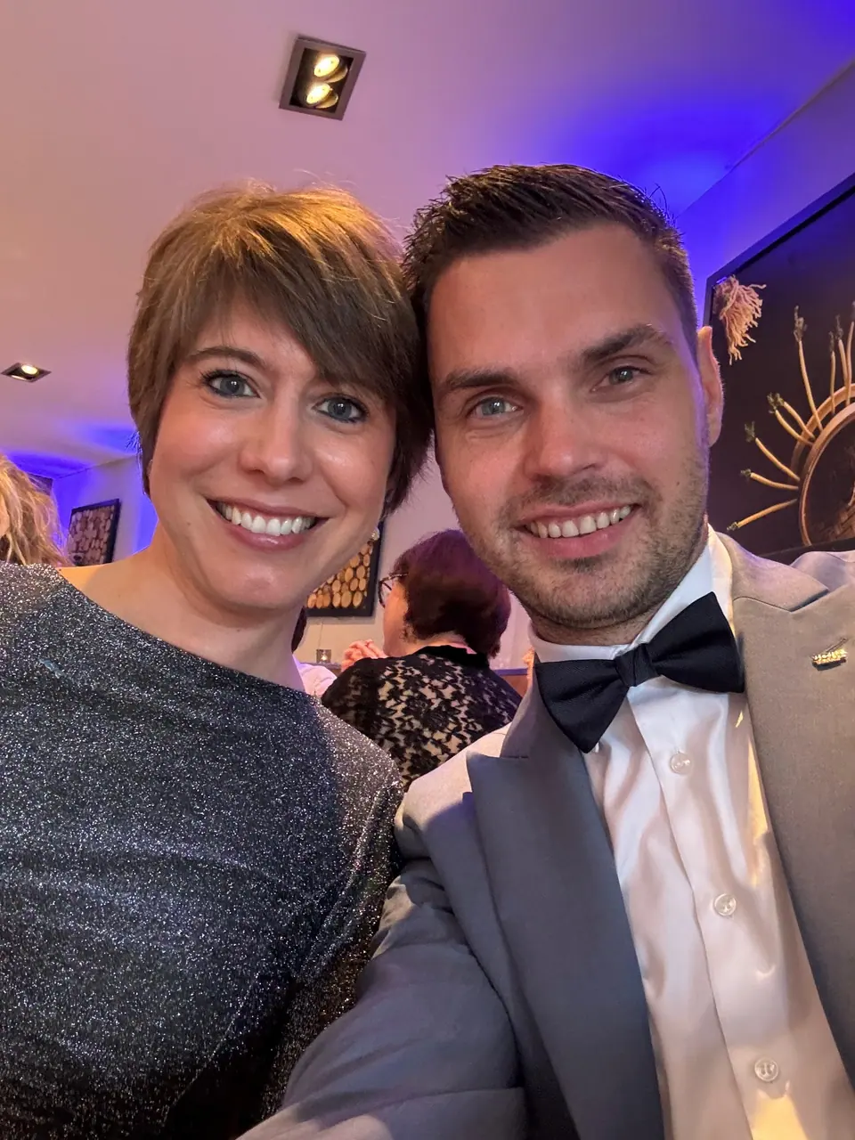 A woman and a man in a bow tie taking a selfie at an evening event