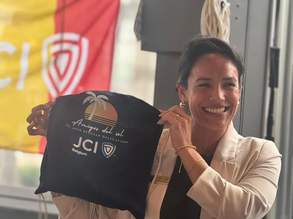 A smiling woman holding up a JCI Belgium tote bag