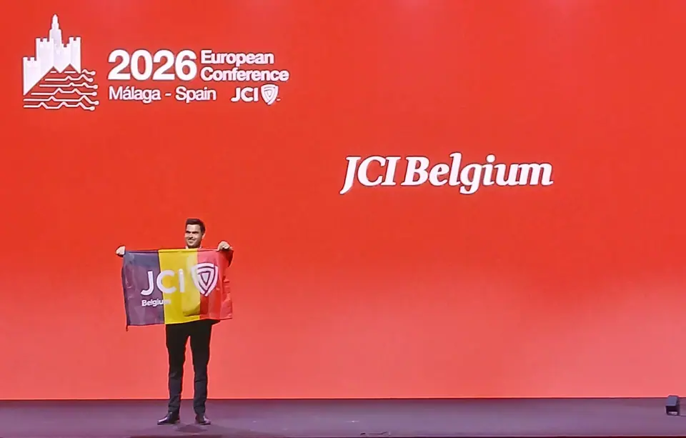 A man holding a Belgian flag on stage in front of a red JCI Belgium screen at the 2026 European Conference