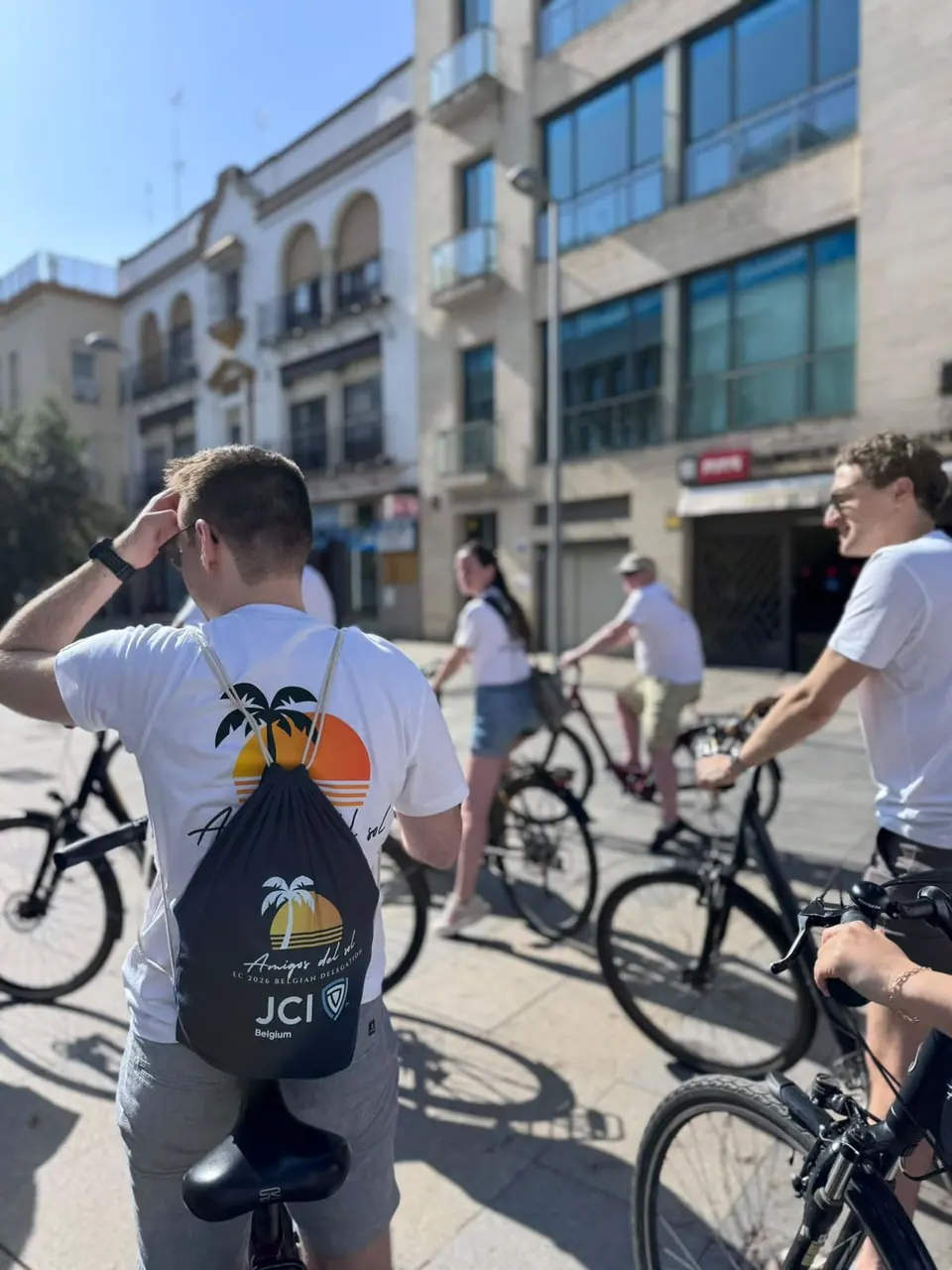 A cyclist seen from behind wearing a JCI Málaga backpack on a city street