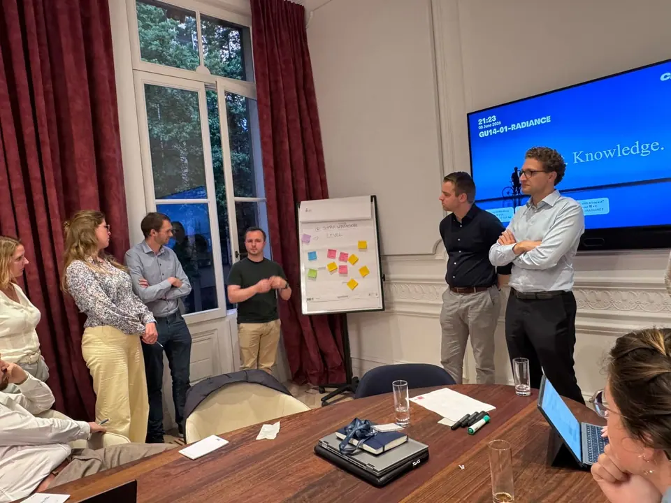 People talking in a meeting room with a flip chart of sticky notes and a screen on the wall