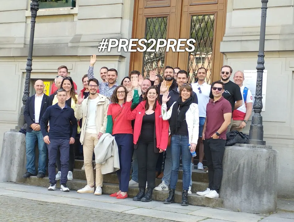 A large group posing on the steps of a stone building under a #PRES2PRES banner