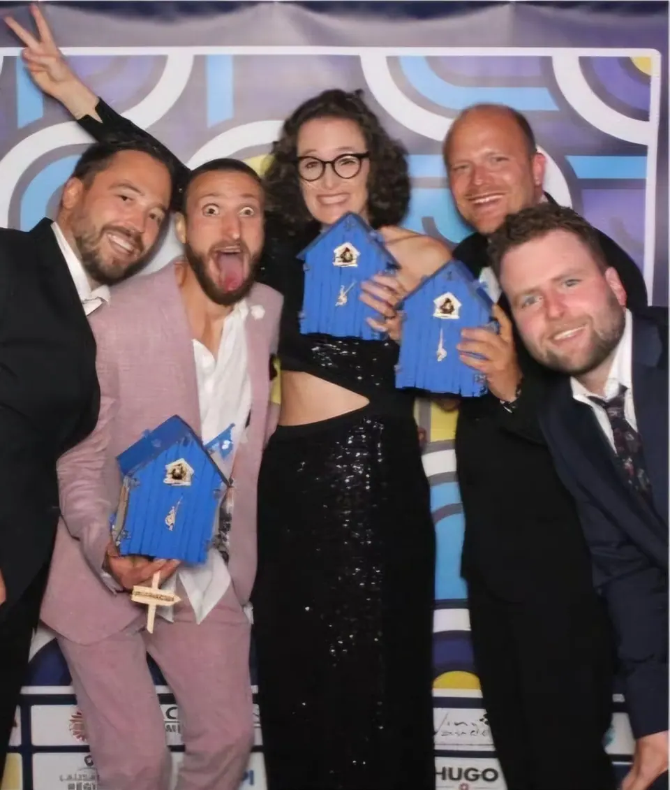 Four people in evening wear laughing and holding blue award trophies in front of a colourful backdrop