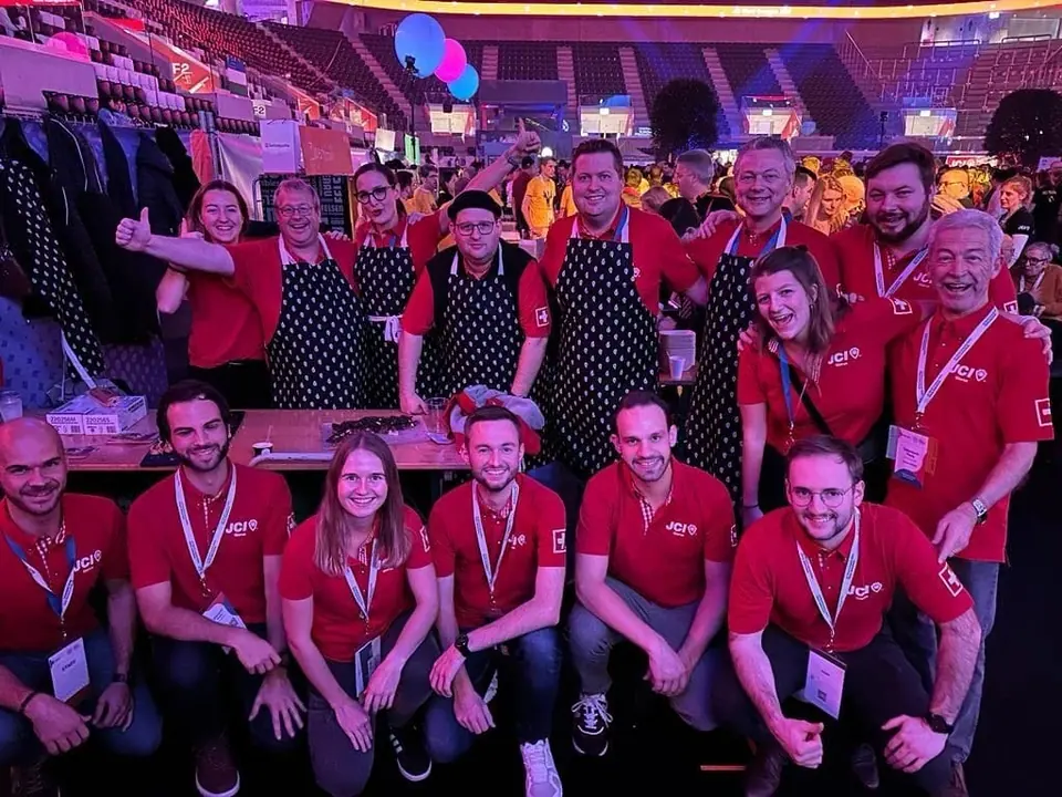A large group in red volunteer T-shirts and aprons smiling at the camera in an event hall