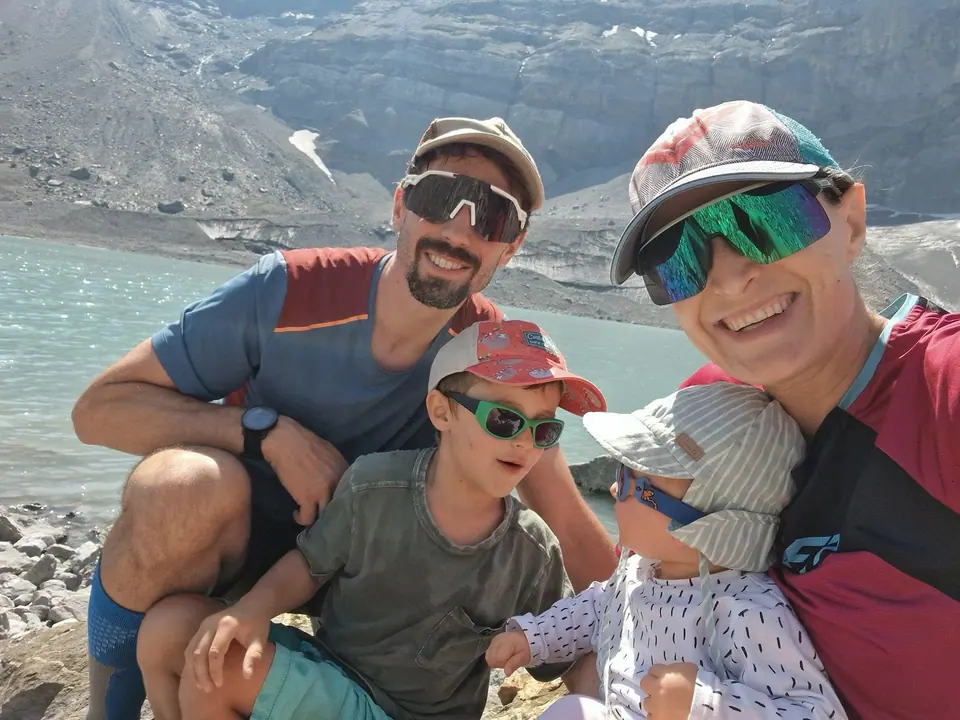 Catia and her family wearing sunglasses and caps in front of a mountain lake