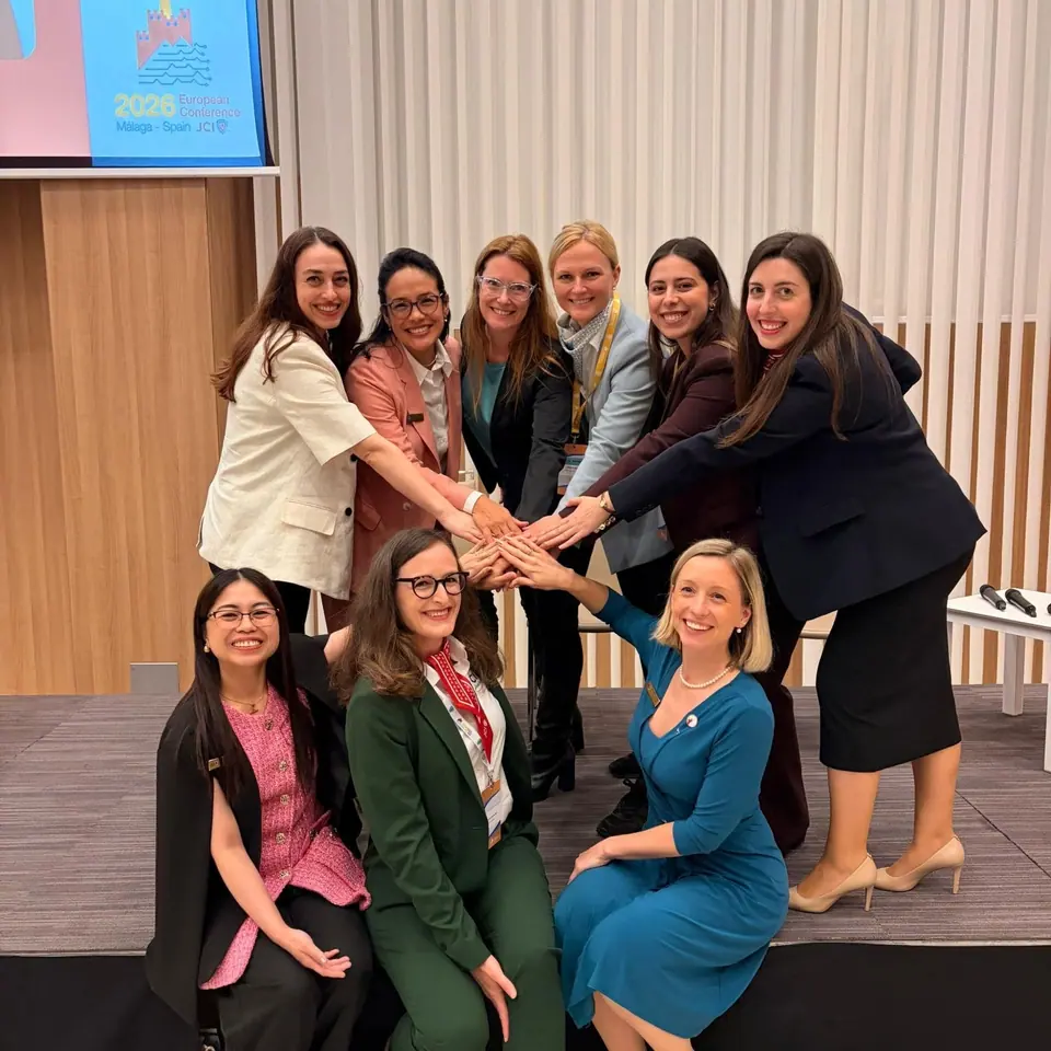 A group of women in business attire joining hands in a circle on a stage
