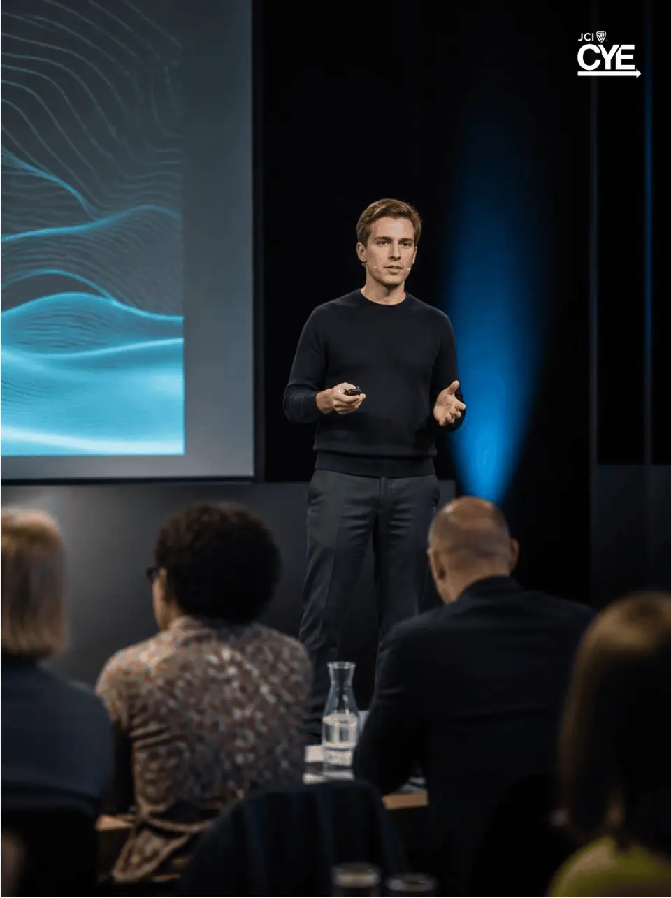A speaker presenting on stage to a seated audience